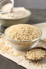 Brown rice, flour and sieve on grey table, closeup