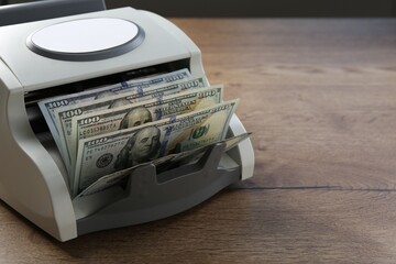 Money counter machine with dollar banknotes on wooden table, closeup. Space for text