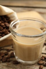 Coffee cream liqueur in glass and beans on wooden table, closeup