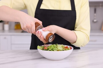 Woman salting tasty salad at white marble table in kitchen, closeup