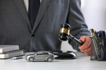 Auto accident law. Man striking gavel at table indoors, focus on toy car