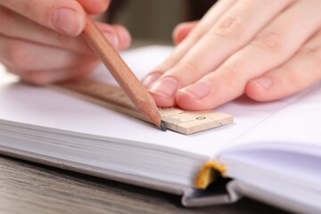 Woman drawing sketch with ruler and pencil on notebook at wooden table, closeup