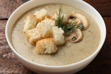 Delicious mushroom cream soup with croutons and dill on wooden table, closeup