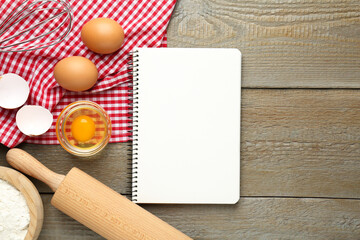 Blank recipe book, eggs and rolling pin on wooden table, flat lay