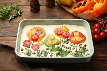 Raw focaccia with vegetables and spices on wooden table