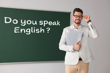Teacher near green chalkboard with phrase Do You Speak English? in classroom