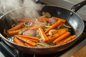 A pan of food is cooking on a stove, with a lot of onions and carrots