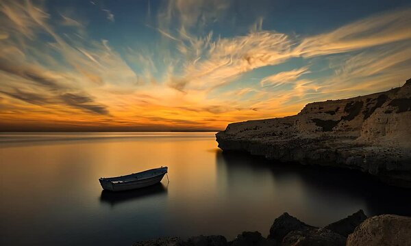 Tranquil seaside scene A small boat rests on calm waters at sunset, framed by striking cliffs under an orange-streaked sky