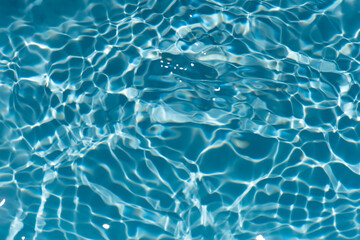 Blue water with ripples on the surface. Defocus blurred transparent blue colored clear calm water surface texture with splashes and bubbles. Water waves with shining pattern texture background.