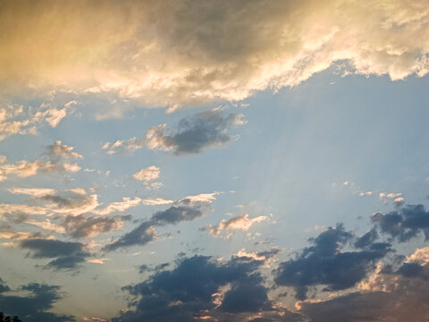 A sky scene with a mix of fluffy clouds and scattered darker clouds. The sky displays a gradient from soft golden tones to light blue, indicating a likely sunset or sunrise setting.