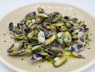 Almejas al ajo y perejil en un plato sobre fondo blanco. Mariscos.