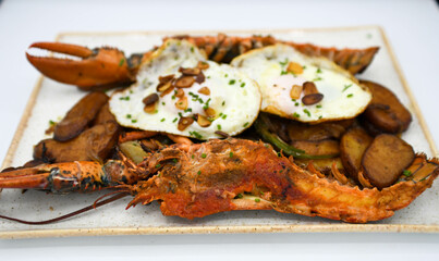 Langosta con patatas y huevo frito en plato blanco.