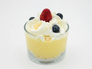 Pudín de vainilla con crema batida y bayas frescas en un vaso sobre fondo blanco