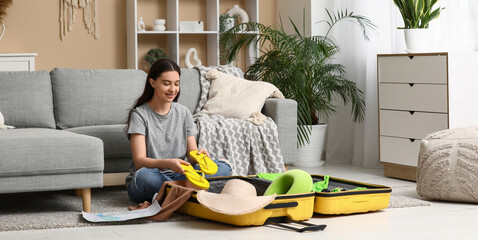 Young woman packing flip-flops in suitcase on floor at home. Summer travel concept