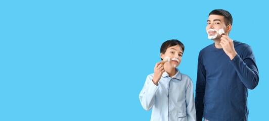 Man and his little son applying shaving foam onto faces against blue background with space for text