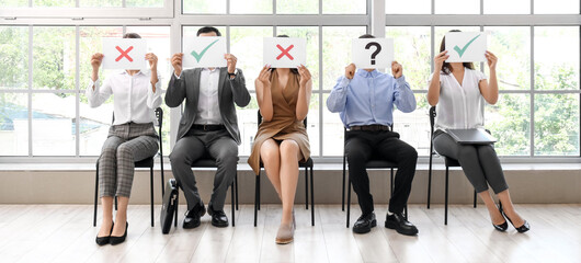Young people holding paper sheets with different marks while waiting for job interview in office