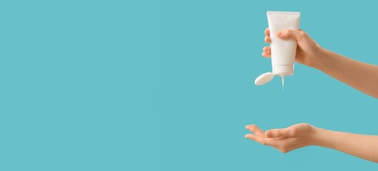 Hands of woman with sunscreen cream on blue background with space for text