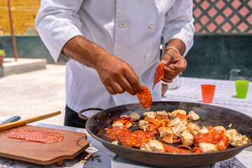 Chef adding chorizo to paella with chicken on a terrace