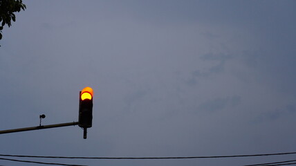 Glimmering hold: an orange traffic signal glows under a grey sky