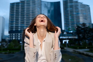 Fototapeta premium Woman laughing joyfully outdoors in business attire with city skyscrapers background, happiness, confidence, urban lifestyle, professional woman