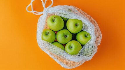 Green apples in reusable bag, orange background, healthy food