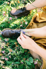 Mom hands insert wildflowers into the shoes on the little girl feet. Cropped