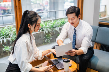 Asian colleagues collaborate on a project at a cafe using a laptop and review documents together