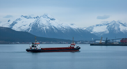 Cargo Ship Sailing on Calm Waters with Snow Capped Mountains in Background Under an Overcast Sky