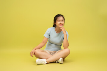 Fototapeta premium Young woman sitting on floor with crossed legs and smiling in a bright yellow background during a casual indoor photoshoot