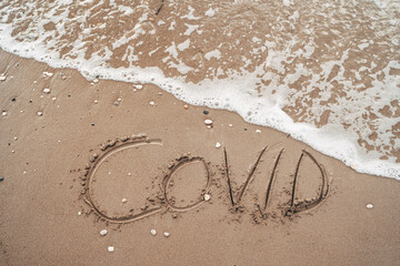 The phrase COVID Written in Sand rests on the Ocean Shore