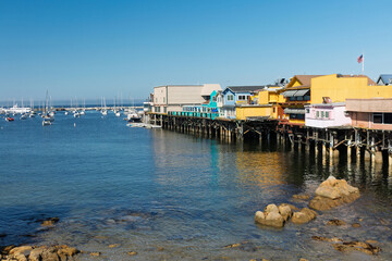 Fototapeta premium A scenic view of Fisherman Wharf in Monterey, showing charming stilted buildings above the water and numerous sailboats floating in the calm harbor