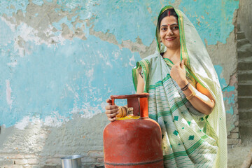 Rural Indian woman with LPG Gas Cylinder for cooking in kitchen. Empowering Women. Clean energy....