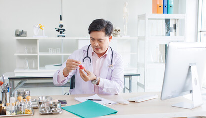 Asian doctor positive confident sitting at desk working physician wearing stethoscope holding bottle of medicine, video online conference computer with patient in clinic hospital medical for wellness
