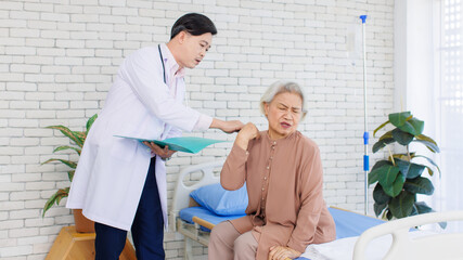 Asian senior woman patient sitting on medical bed holding hand on head complain of headache to...