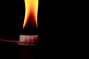 Toothbrush bristles burning on fire on a black background, representing danger and poor hygiene