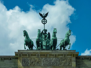 Famous Quadriga statue, depicting goddess Victoria in four-horse chariot, majestically sits atop Brandenburg Gate in Berlin, Germany, under vibrant blue sky dotted with white clouds, an iconic symbol