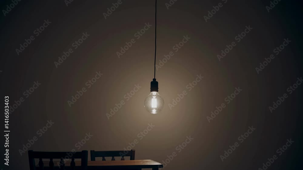 Poster moody video scene with a low-angle shot of a dimly lit bulb over a wooden table and chairs, creating