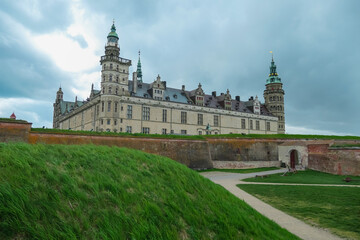 Fototapeta premium Kronborg Castle, the historic setting for Shakespeare's Hamlet, stands majestically behind green grassy ramparts and weathered brick fortifications, its Renaissance towers in Helsingor, Denmark