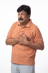 Indian senior man having health issues and body chest pain on white. Elderly asian man standing...