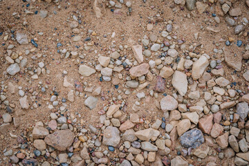 A mix of sand and small to medium-sized natural stones and pebbles scattered across the ground, forming a rough, earthy textured surface..