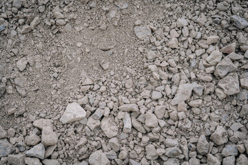 Dusty gray crushed stones and fine gravel mix spread on the ground, forming a rough, uneven surface...