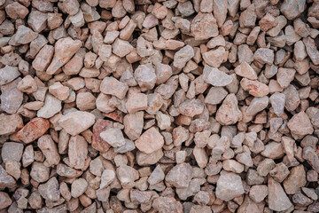 Close-up view of large, rough, irregular brown and gray stones piled together, often used for road base or construction foundation..