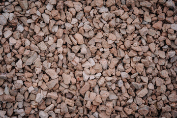 Close-up of rough, dusty brown and gray crushed stones used for construction, forming a rugged and...