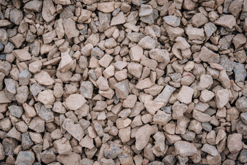 Rough pile of dusty, angular gray and brown crushed stones forming a coarse, natural texture suitable for construction or landscaping purposes..