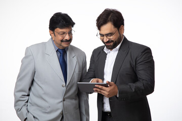 Indian successful businessman using digital tech tablet while standing inside office. Two businessmen watching tablet feeling happy for trade stock, Business growth concept, marketing strategy 