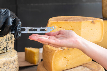 A vendor slices a piece of cheese with a knife at a farmers market