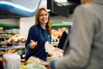 Happy cashier talking to customer at supermarket checkout.