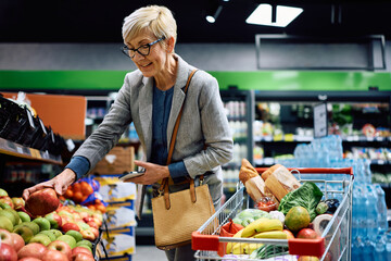 Happy senior woman buying fresh fruit at supermarket.