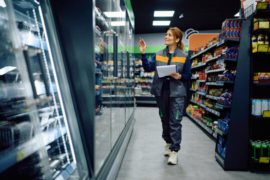 Happy supermarket manager examining stock of supplies at refrigerated section.