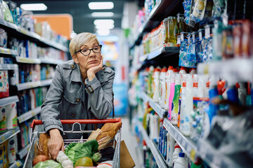 Senior woman feeling worried about increase of prices while buying in supermarket.